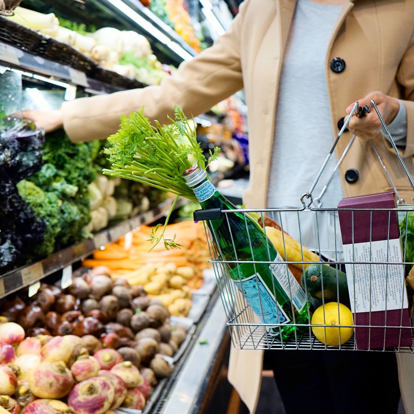 Shopper selecting fresh produce with a full grocery basket